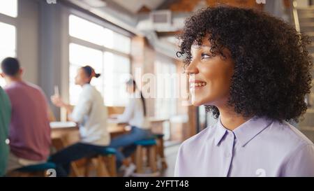 Smiling Businesswoman Working In Busy Open Plan Office With Colleagues In Background Stock Photo