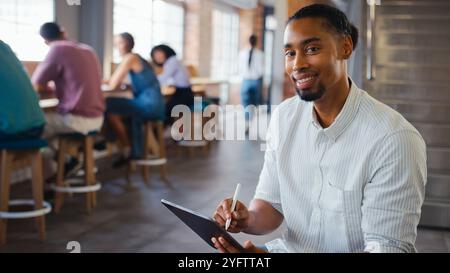 Portrait Of Businessman Using Digital Tablet And Stylus Pen In Office With Colleagues In Background Stock Photo