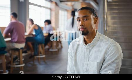 Portrait Of Serious Young Businessman Working In Busy Modern Office With Colleagues In Background Stock Photo