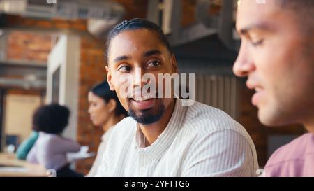 Two Businessmen Meeting In Office Discussing Documents With Colleagues In Background Stock Photo