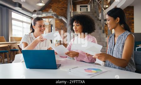 Three Young Businesswomen Meeting In Modern Office Sitting Around Table Working On Laptop Together Stock Photo