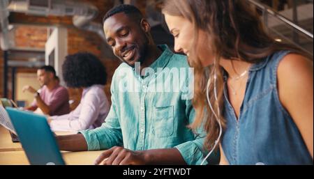 Male And Female Businesspeople Meeting In Office Working On Laptop With Colleagues In Background Stock Photo