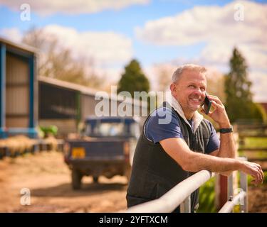 Mature Male Farm Worker Standing Outside Barn Making Call On Mobile Phone Stock Photo