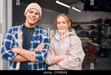 Portrait Of Smiling Male And Female Workers Standing In Doorway Of Concrete Workshop Stock Photo