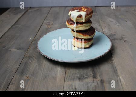 Condensed milk, sweet sauce, flows down homemade pancakes, cheesecakes on a plate. Homemade food. Stock Photo