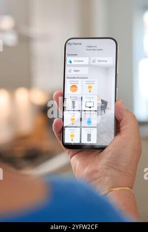 A person is viewing a home automation application on their smartphone within a stylish and contemporary kitchen. The screen shows various options for Stock Photo