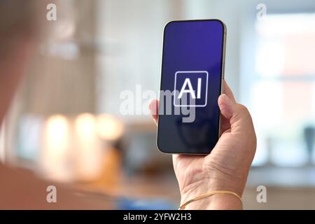 A person is holding a smartphone displaying the text AI on the screen, highlighting the significance of artificial intelligence technology. The backgr Stock Photo