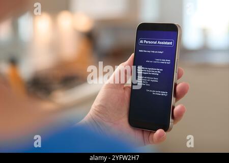 A user interacts with an AI personal assistant on their smartphone in a contemporary kitchen. The screen shows a welcome message, prompting the indivi Stock Photo