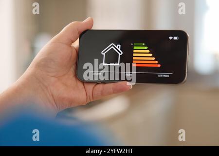 A person holds a smartphone showing an interface for home automation, detailing different energy levels indicated by colored bars. The background sugg Stock Photo