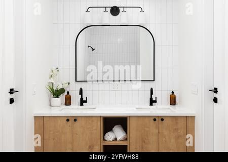 A modern farmhouse bathroom with a white oak cabinet, white marble countertop, vertical subway tile backsplash, and black faucet. Stock Photo