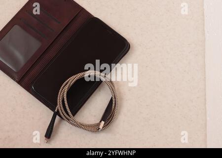 Image of a smartphone in a case-book and a charging cord. Top view. Stock Photo