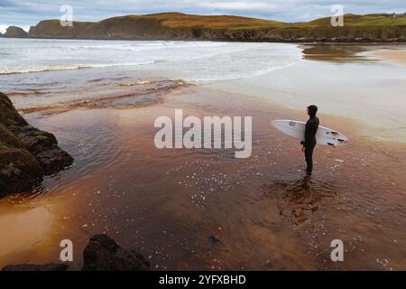 3 Nov. 2024, Farr Bay, Bettyhill, Sutherland, Scotland. A surfer standing on the beach at Farr Bay. The reddish water color is from runnoff from nearb Stock Photo