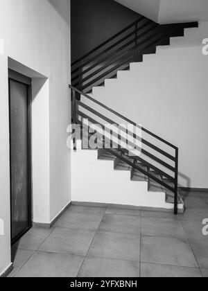 Choose Your Path: Staircase or Elevator in the Lobby  left Corner, A Moment of Decision.  Black and white. Stock Photo