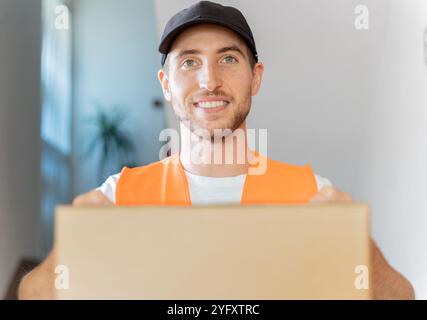 Close-up of an attractive delivery man with cardboard box in his hands. Home delivery of a package in customer home Stock Photo