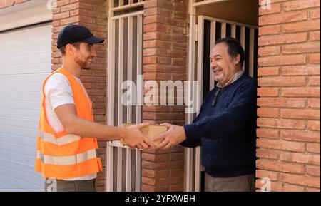 Young man working as a delivery man delivering a box to customer at home. Friendly worker smiling to customer. Stock Photo