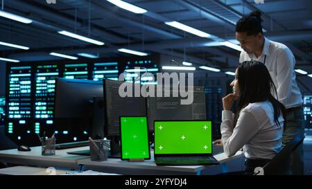 Engineers in data center monitoring security threats using chroma key devices. Experts using isolated screen tablet and laptop, ensuring compliance with regulations, camera B Stock Photo
