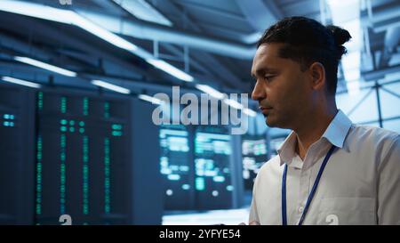 Software developer walking in data center, managing and maintaining databases, ensuring data integrity and security. Close up of man updating server room mainframe systems using tablet, camera B Stock Photo