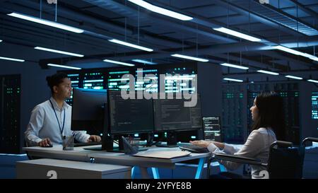 Person with paraplegia working in inclusive server hub workspace, typing on PC. Woman in wheelchair doing tasks in data center housing advanced data storage infrastructure, camera B Stock Photo