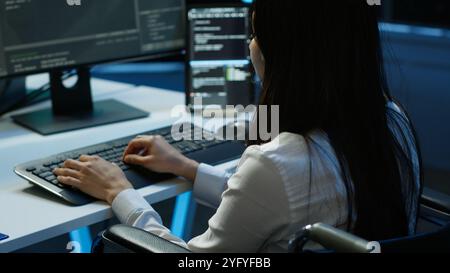 Person with paraplegia working in inclusive server hub workspace, typing on PC. Woman in wheelchair doing tasks in data center housing advanced data storage infrastructure, camera A Stock Photo