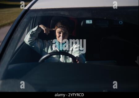 Caucasian woman twirls finger at temple while driving.  Stock Photo