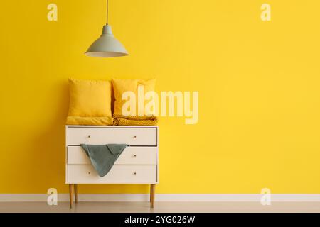Pillows with folded blankets on commode near yellow wall in room Stock Photo