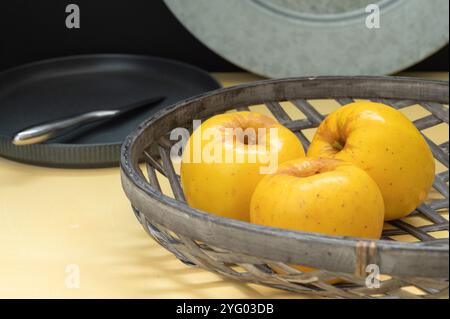 Three opal apples sit in a basket on a yellow table. Stock Photo