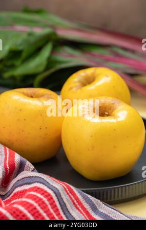 Three yellow Opal apples on a table with swiss chard leaves in the background. Stock Photo