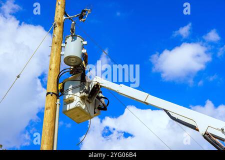 Transformer other electrical components are seen mounted on wooden utility pole, with maintenance underway. Stock Photo