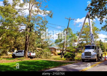 An elevated platform holds worker performing maintenance on transformer attached to wooden pole. Stock Photo