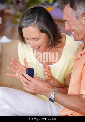 Senior couple, surprise and engagement proposal in home for relationship, commitment and romance. Elderly people, happy and excited for hand in Stock Photo
