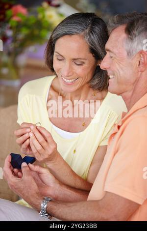 Elderly couple, ring and engagement proposal in home for relationship, commitment and romance. Senior people, happy and jewelry for hand in marriage Stock Photo