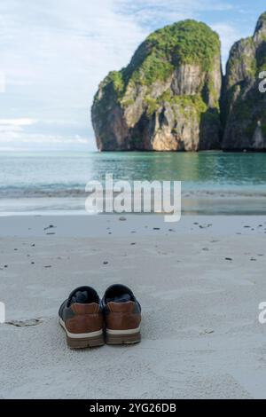 Shoes stand on the empty sandy beach in front of a landscape with rocks in thailand Stock Photo