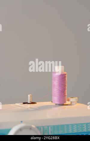 View of a sewing machine with a spool of pink thread placed on top Stock Photo