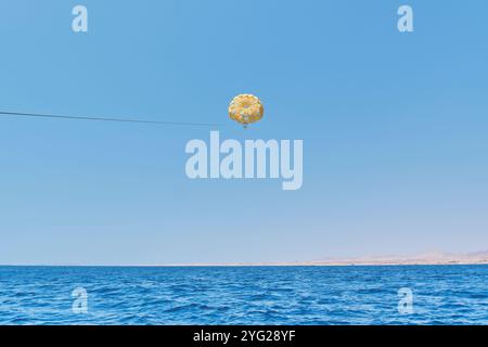 Senior white woman with gray hair under yellow dome of parachute enjoying parasailing against blue sky, Red Sea and egyptian coast. Extreme entertainm Stock Photo