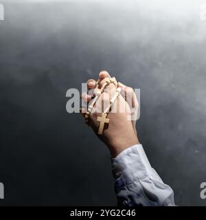 Man raised hand while holding a rosary beads. Symbol of faith and worship in God. People christianity prayer. Religious service, holiday or concept Stock Photo