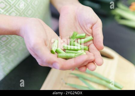 Woman hands holding pieces of fresh green beans in kitchen Stock Photo