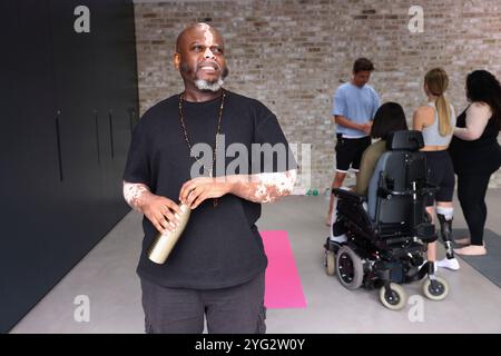 Man with vitiligo standing in gym and looking away, people in background Stock Photo