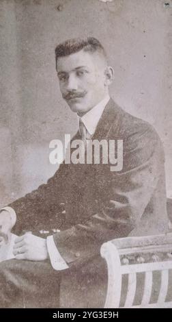 Budapest, Austro-Hungarian Empire, circa 1905: An elegant studio portrait of a young man with a classic Hungarian mustache. He is wearing a formal suit with a high starched collar and sitting in a luxurious upholstered tub chair. A prime example of urban bourgeois fashion in Hungary at the turn of the century. Stock Photo