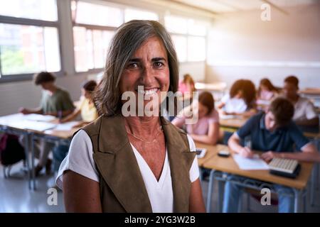 Portrait of happy mature Caucasian female teacher at high school posing in class with confidence. Stock Photo