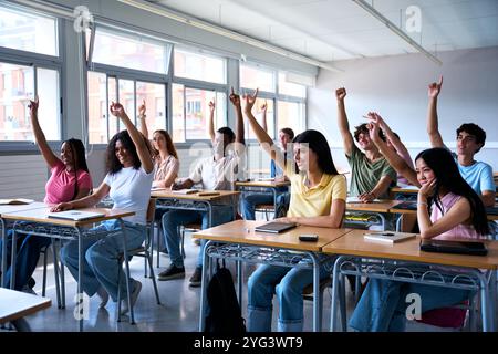 Happy group of multi-ethnic students sitting in classroom with hands raised. High school concept Stock Photo