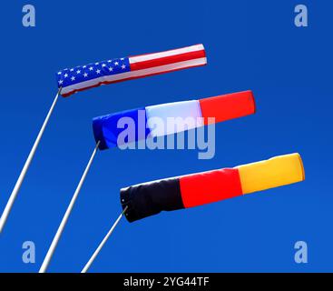 three windsocks in strong winds, in the colours of the national flags of the USA, France and Germany against a blue sky Stock Photo