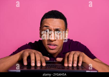 Photo portrait of attractive young man typing keyboard confused face dressed stylish violet clothes isolated on pink color background Stock Photo