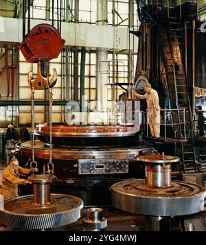 Huge gear cylinders, some being moved by crane, at a Vickers engineering factory c. 1970. Vickers was a UK engineering company that existed from 1828 until 1999. It began in Sheffield as a steel foundry, famous for casting church bells. It branched out into military equipment and shipbuilding. In 1911 it expanded into aircraft manufacture, and later into electricals and railways. After World War II Vickers-Armstrong made commercial aircraft, including the VC10 jet in 1959. In the 1960s parts of Vickers were nationalised, and in 1999 the rest of the company was acquired by Rolls-Royce. Stock Photo