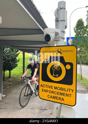 A cyclist with helmet on head cycle through the shelter path while an LTA active mobility enforcement camera is monitoring the walkway, Singapore. Stock Photo