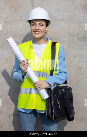 Portrait of a Confident female architect smiling and holding blueprints on a construction site, showcasing expertise and professionalism in the buildi Stock Photo
