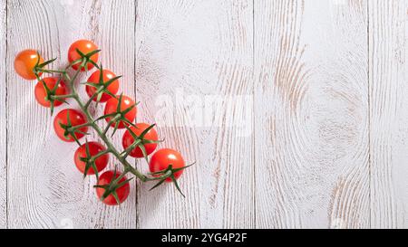Flatlay cluster of cherry tomatoes on the vine rests on a textured white wooden surface, highlighting the contrast between the bright red tomatoes and Stock Photo