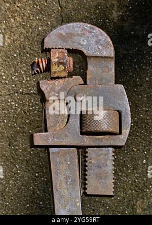 A close up of an Old rusty Vintage plumbers pipe wrench. On a cemment background. With a broken bolt in the teeth. Stock Photo