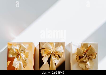 Three Christmas gift boxes, adorned with vibrant golden ribbons on white background with shadows. Flat lay. Copy space Stock Photo