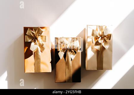 Three Christmas gift boxes, adorned with vibrant golden ribbons on white background with shadows. Flat lay. Copy space Stock Photo