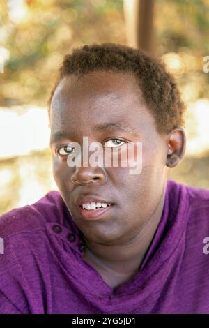 headshot portrait of village African chubby woman with short hair sited outdoors in the yard Stock Photo